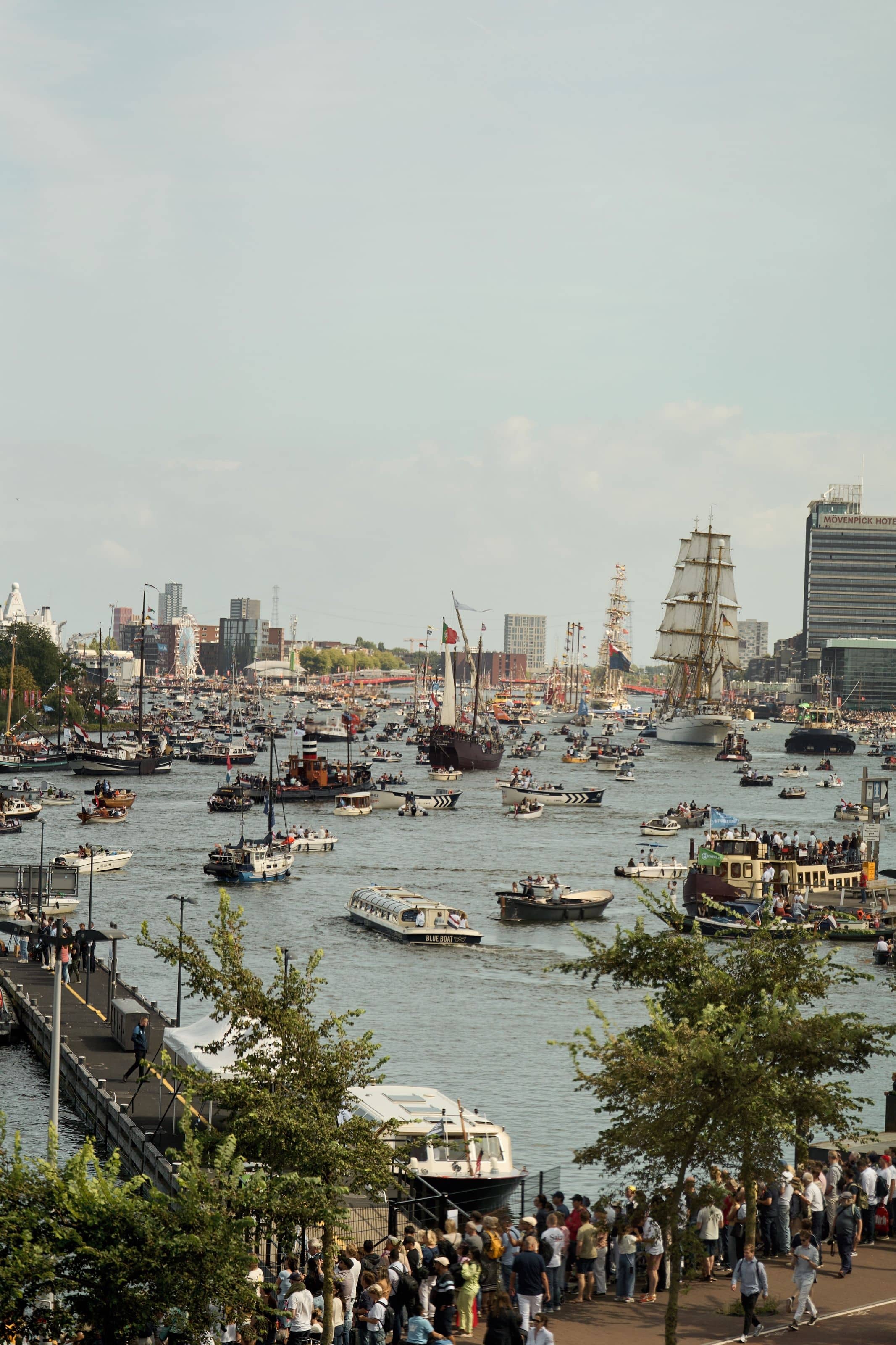 The IJ filled with hundreds of small boats, a tall ship under sail in the distance beside the Mövenpick hotel