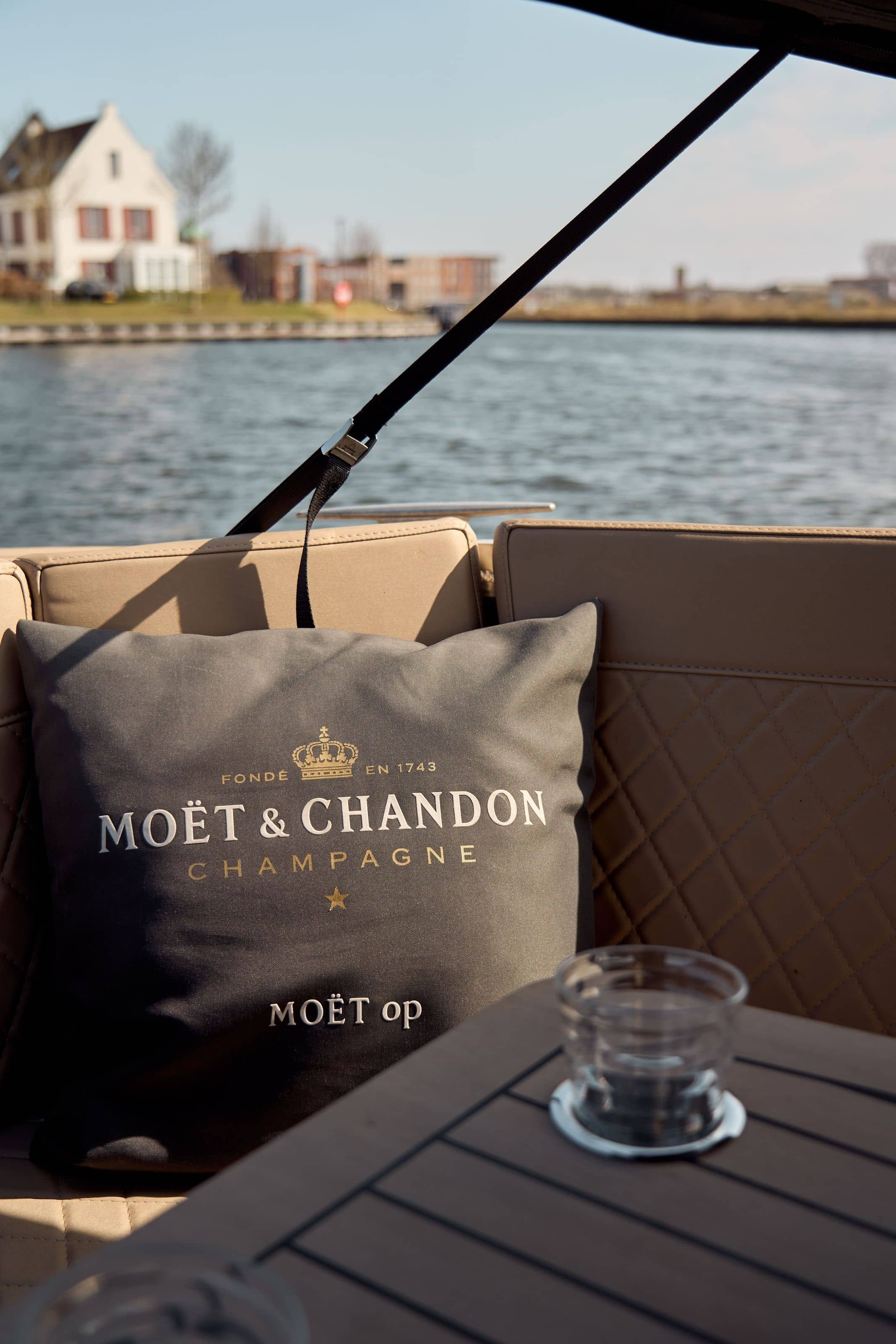 View from aboard across the water to the Harderwijk waterfront, a gabled house on the shore, a Moët & Chandon cushion and two glasses on the boat’s table