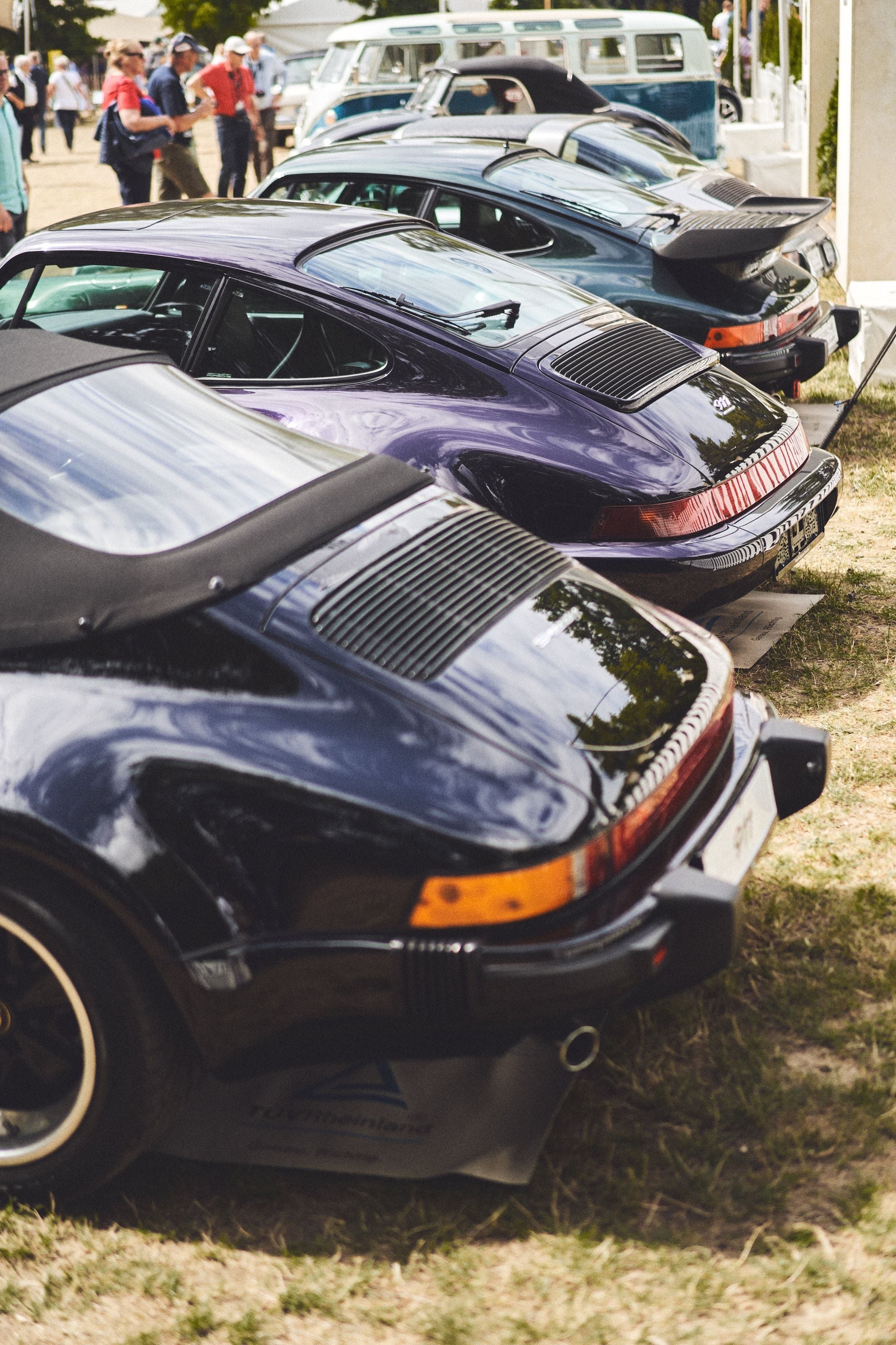 A line of Porsche 911s parked at an angle, their rear ends receding into the distance, a VW camper van behind them