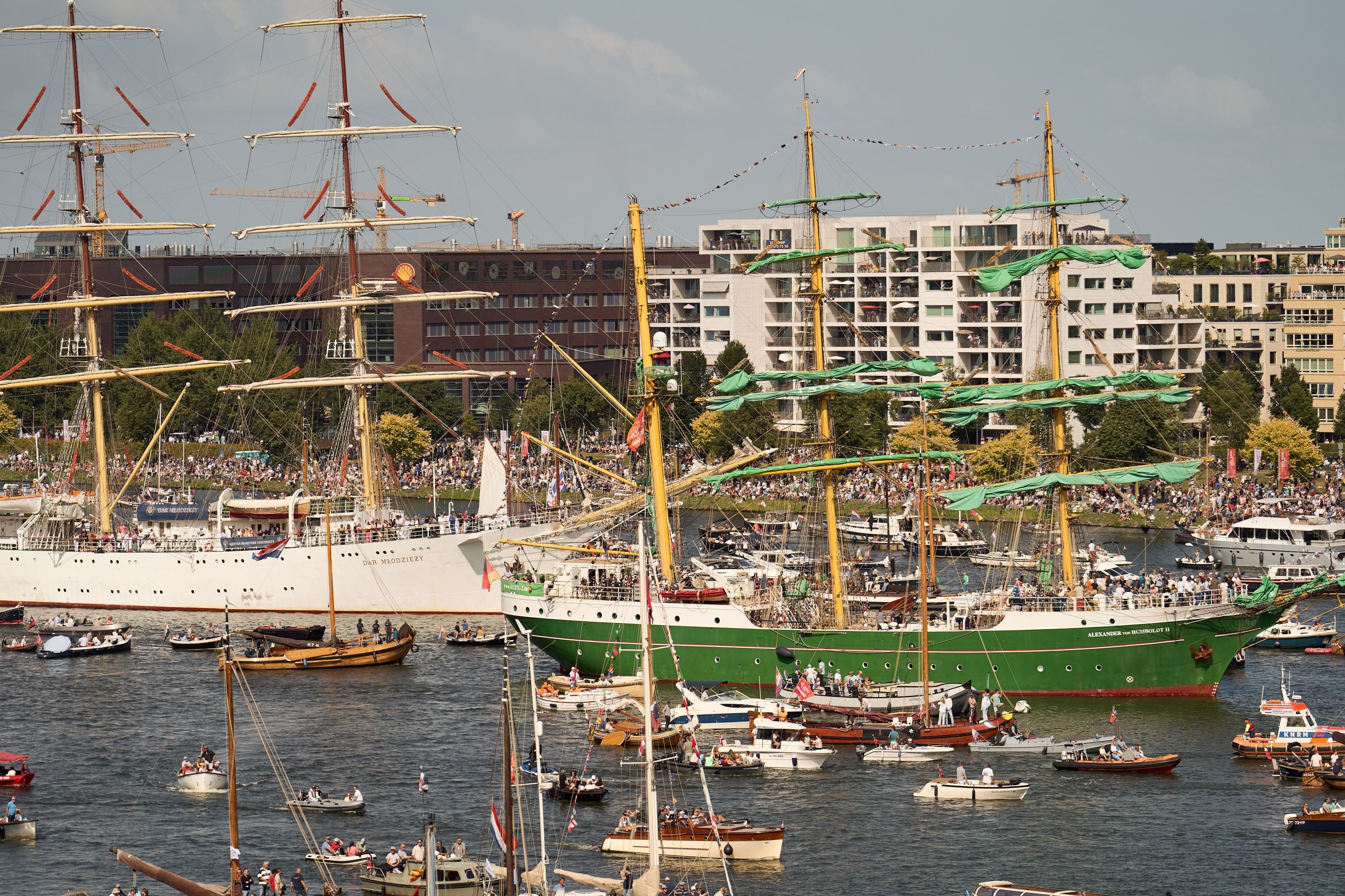 The tall ships Dar Młodziezy and the green-hulled Alexander von Humboldt II lying in the IJ, sails furled in green covers, spectators packed on the bank behind