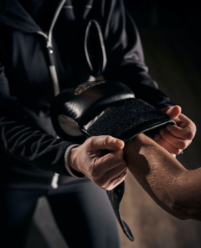 Close up of a trainer's hands fastening the strap of a boxing glove around a wrist