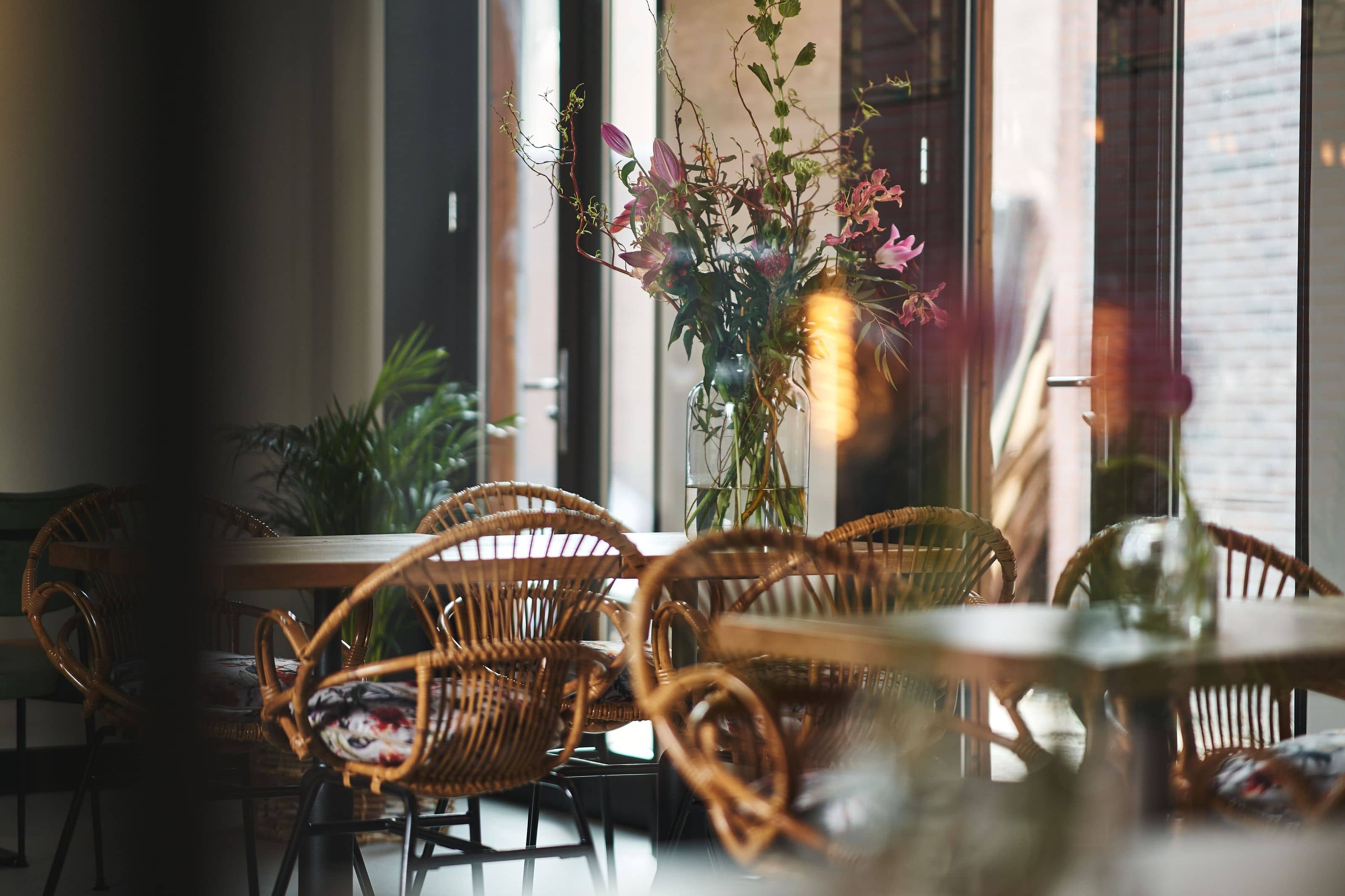 Rattan chairs at tables in the window, a tall arrangement of pink lilies against the glass