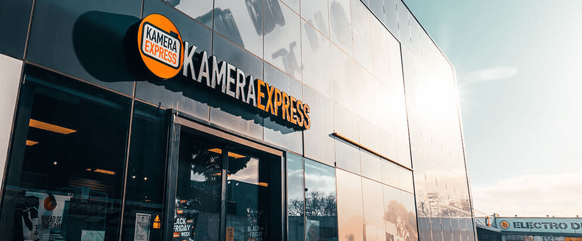 The Kamera Express shopfront in low winter sun, the round orange logo and lettering across a dark tiled facade