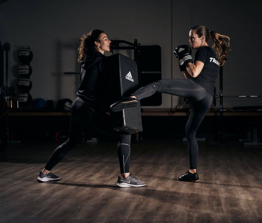 A woman driving a high kick into a strike pad held braced by her trainer