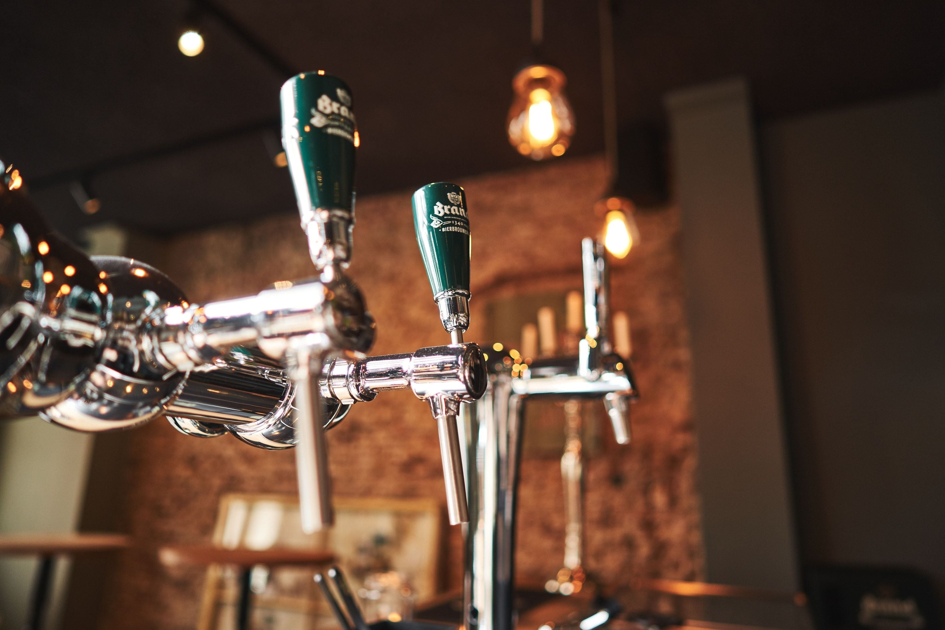 Two Brand beer taps on the counter, filament bulbs and bare brick behind them