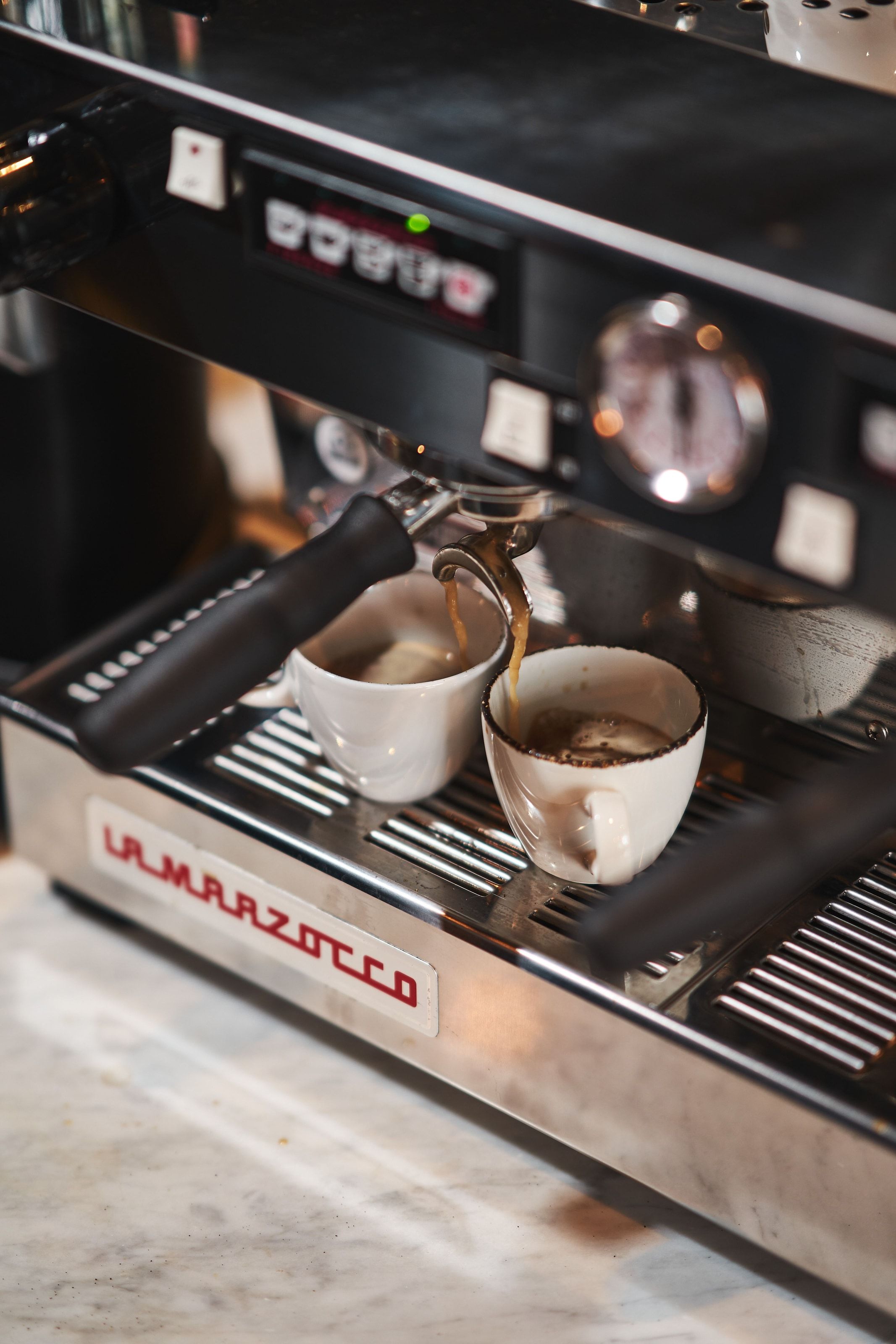 A La Marzocco machine drawing two espressos into white cups on a marble counter