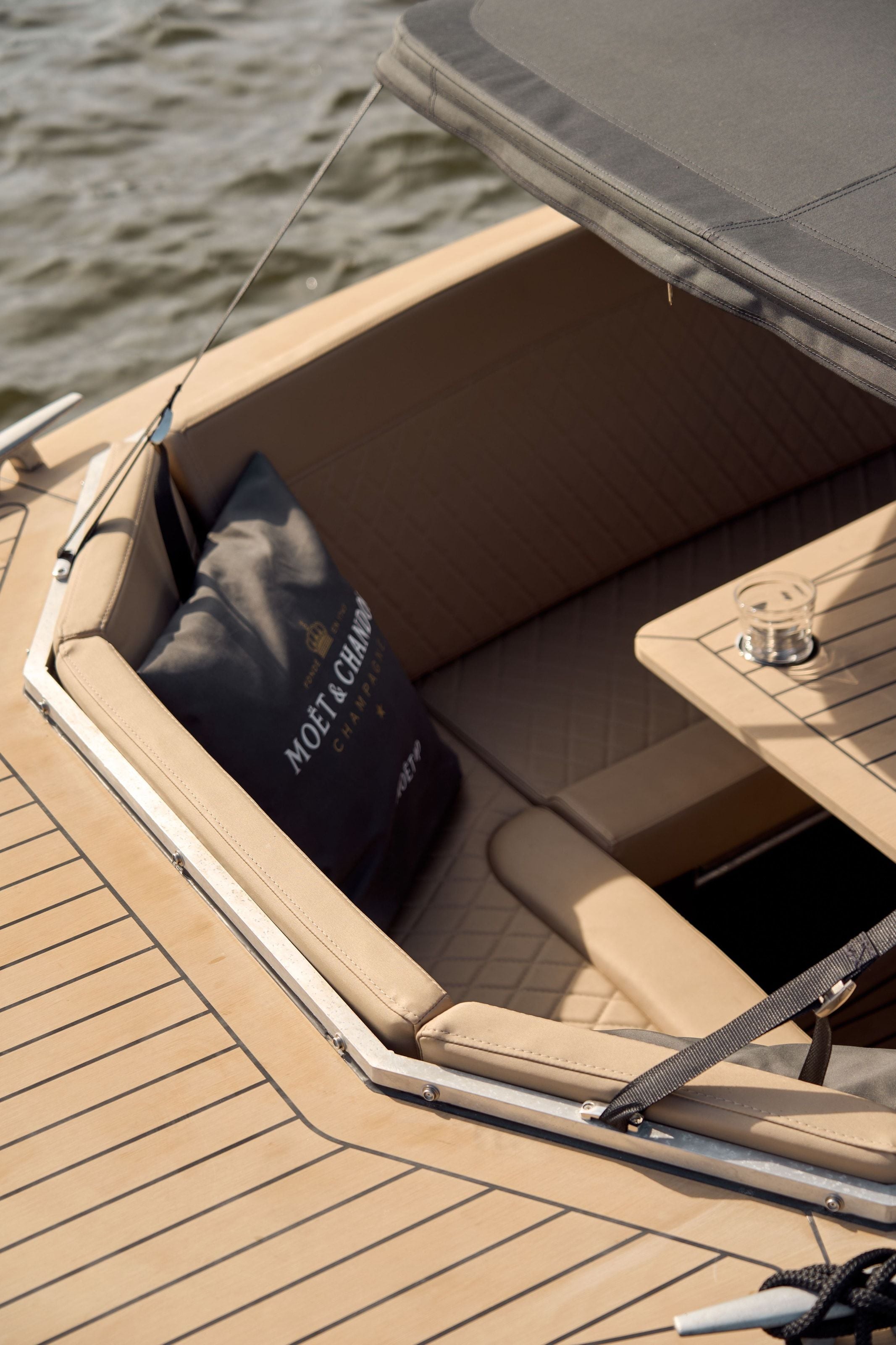 Looking down into the stern seating of the electric boat, teak decking, a cushion tucked against the bimini frame and a drink on the side table