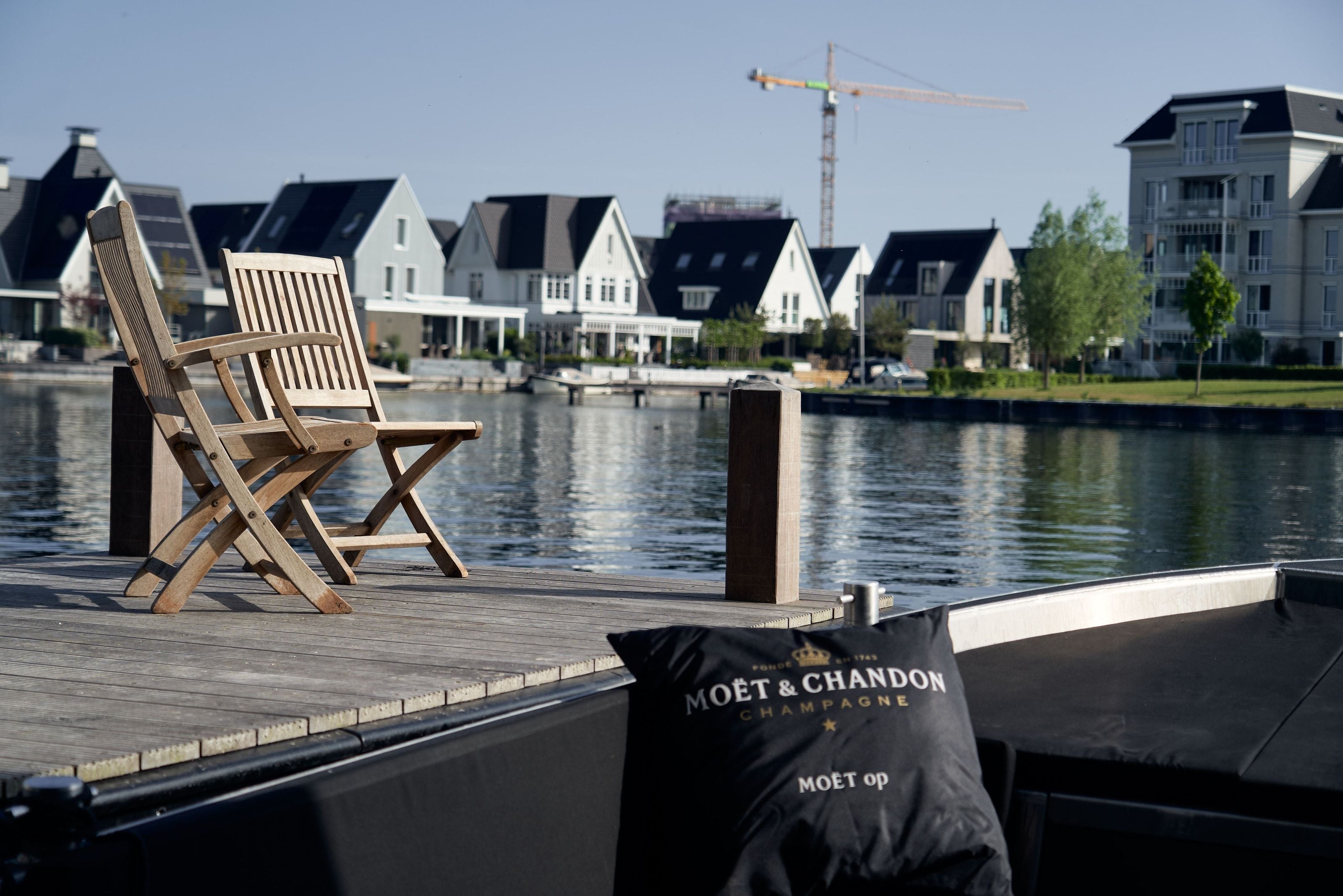 Two teak chairs on the jetty beside a moored boat, the gabled houses across the water in evening light