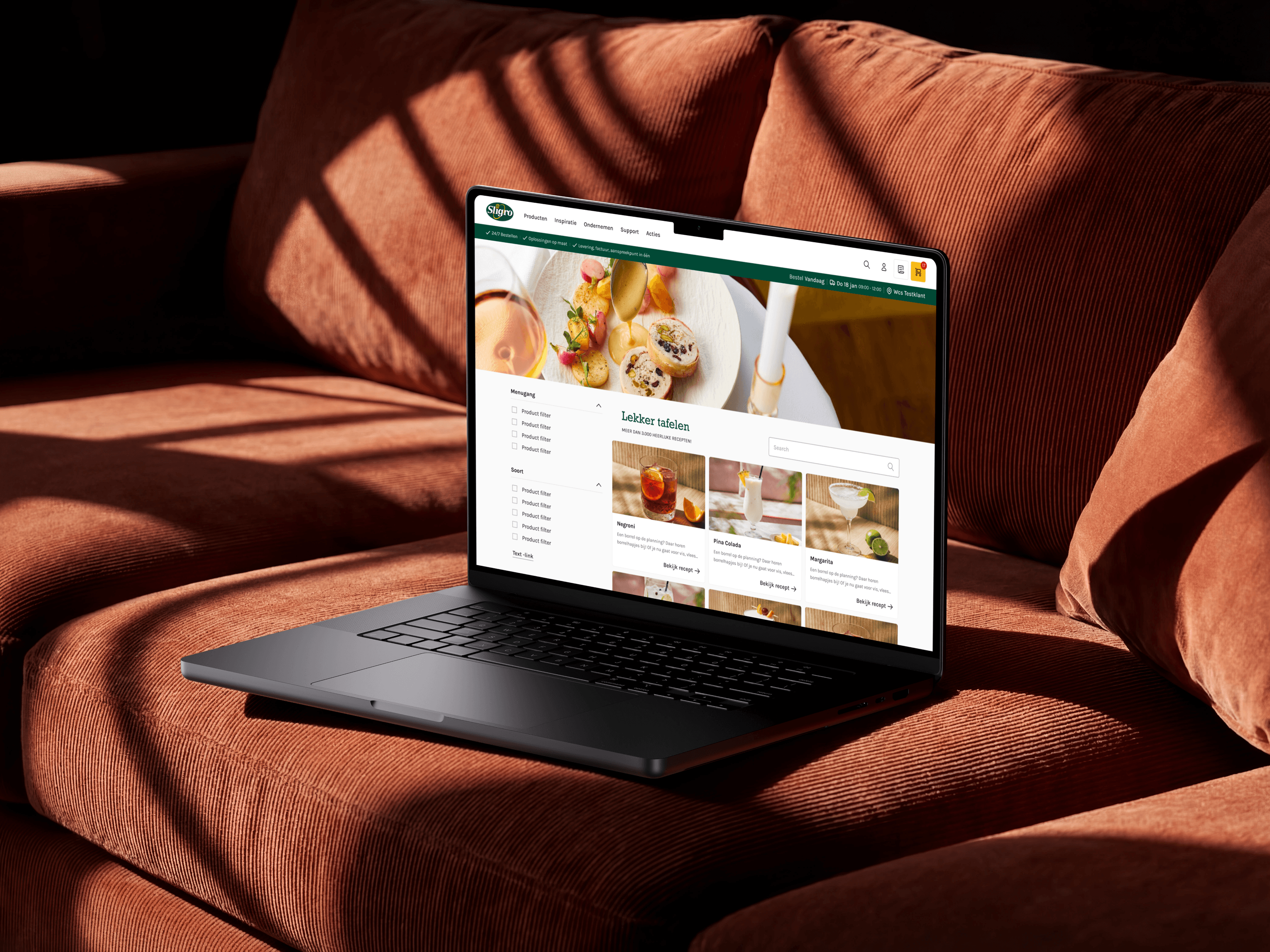 A MacBook on a rust-coloured sofa showing Sligro’s ‘Lekker tafelen’ recipe pages, a plated dish above cocktail cards for a Negroni, Pina Colada and Margarita