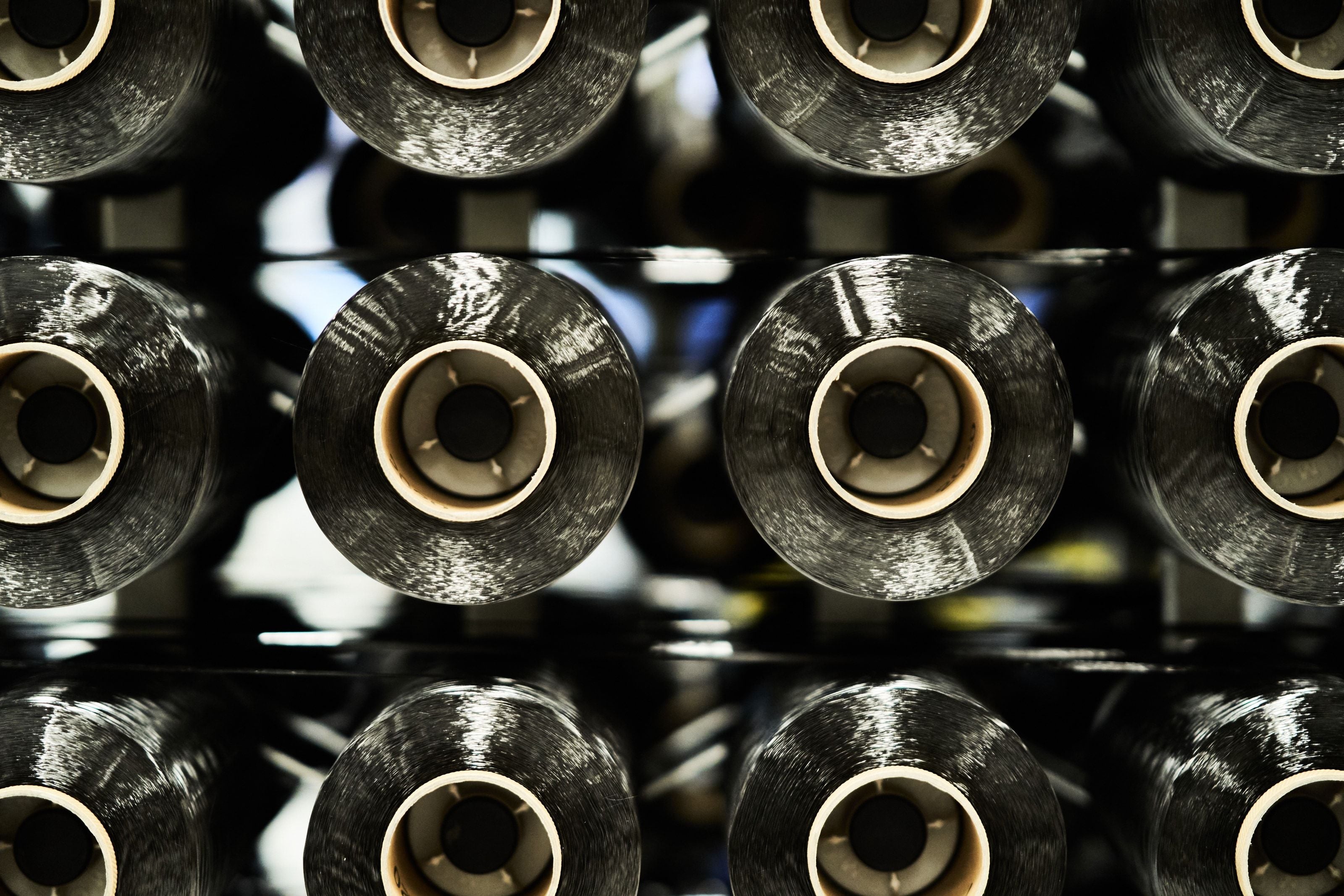 Rows of black carbon-fibre tow spools racked in a production line, seen head-on