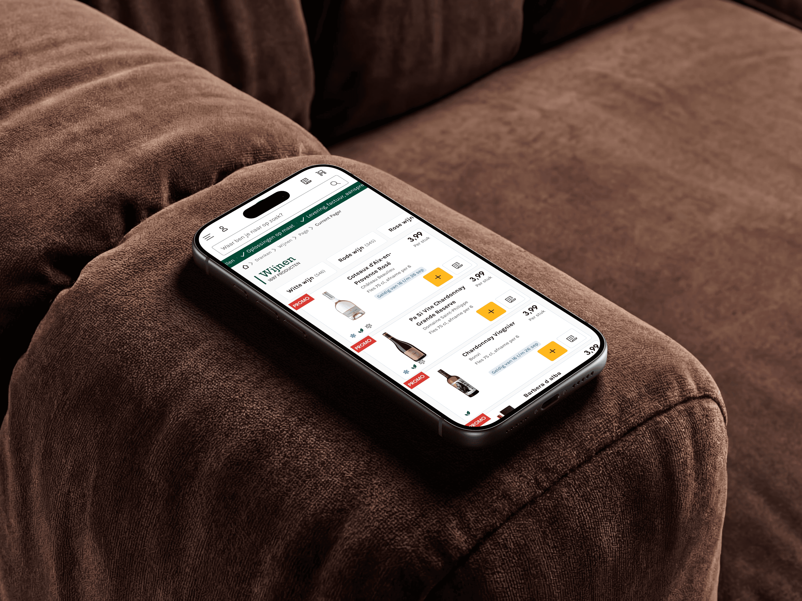 An iPhone lying on a brown sofa arm showing the Sligro wine listing, a promo label and price beside each bottle