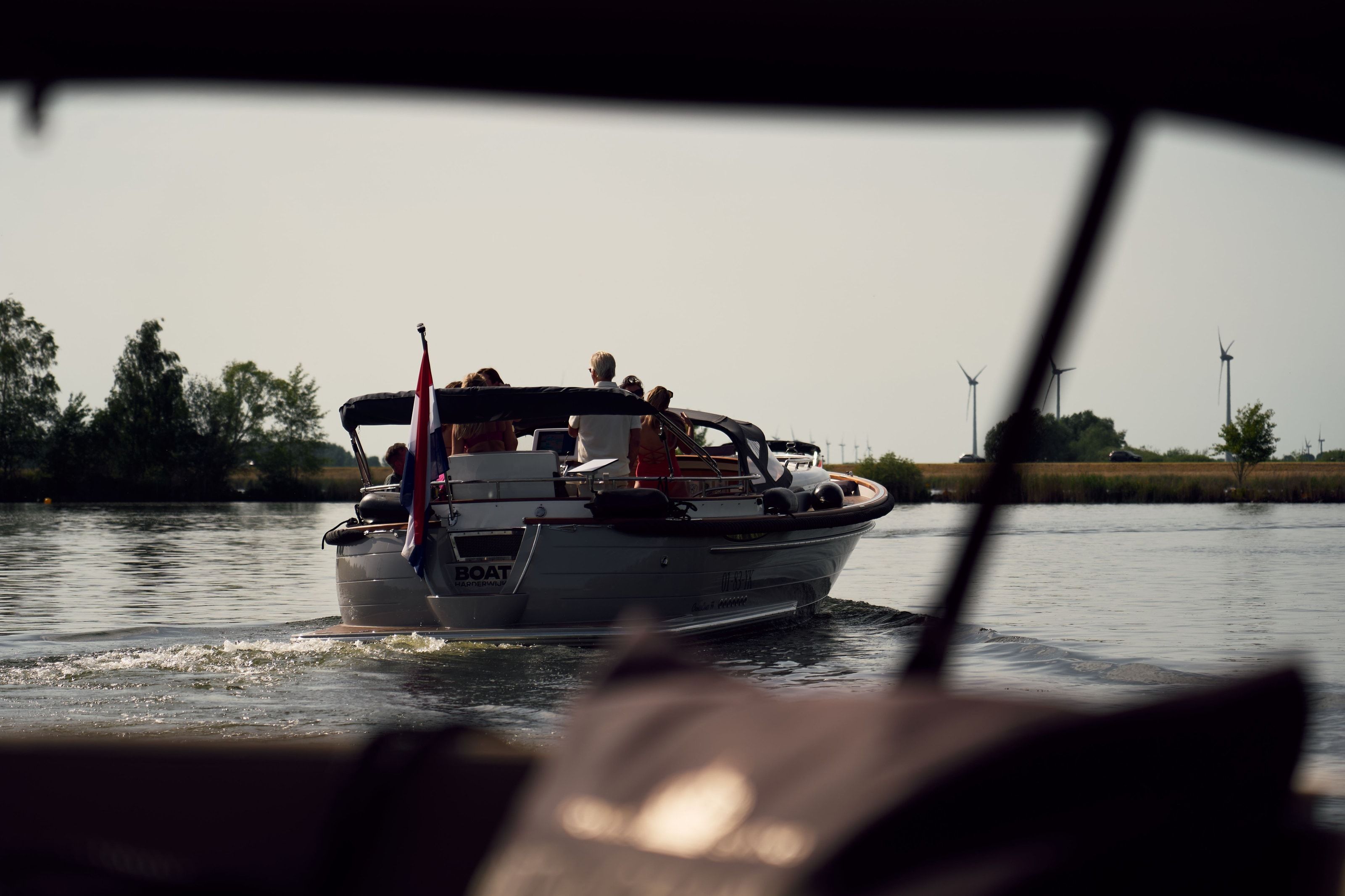 A dark grey electric Crossover boat underway on a canal near Harderwijk, the skipper at the helm under its open bimini