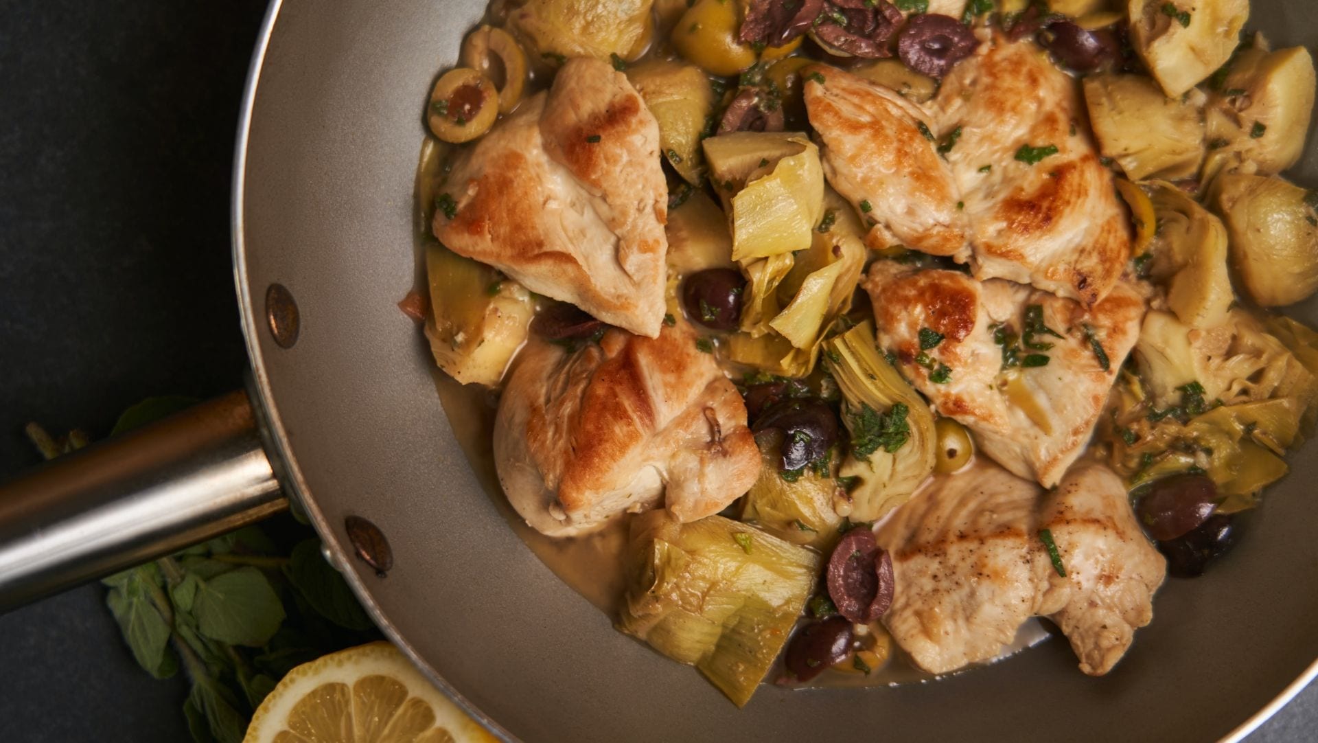 A pan of chicken with artichokes, green and black olives, lemon and oregano