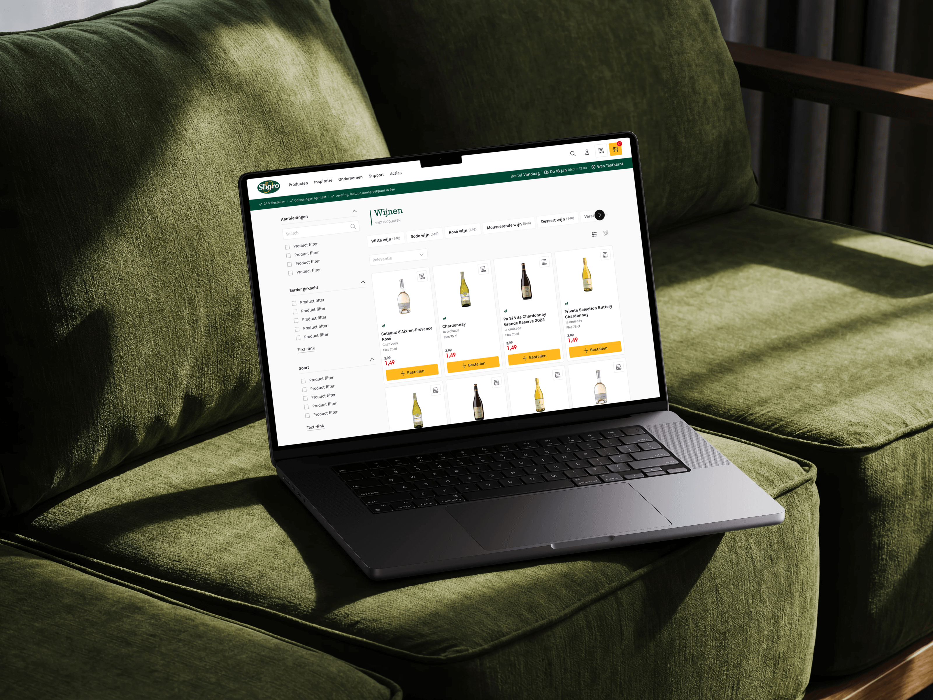 A MacBook on a green sofa showing the Sligro wine category, filters down the left and product cards with order buttons