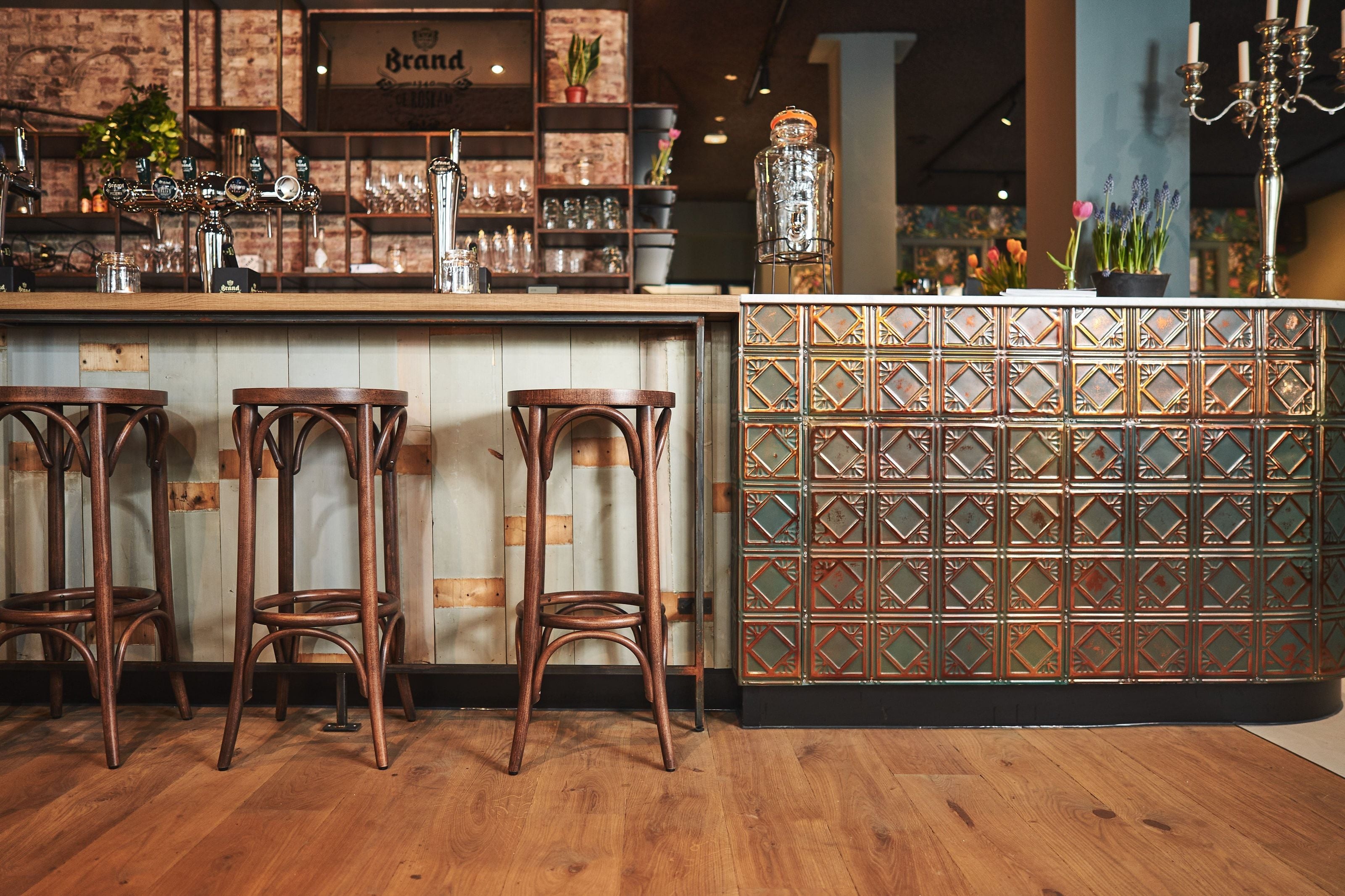 The bar at De Roskam: bentwood stools along a timber counter, its front tiled in green and copper, taps and glassware behind