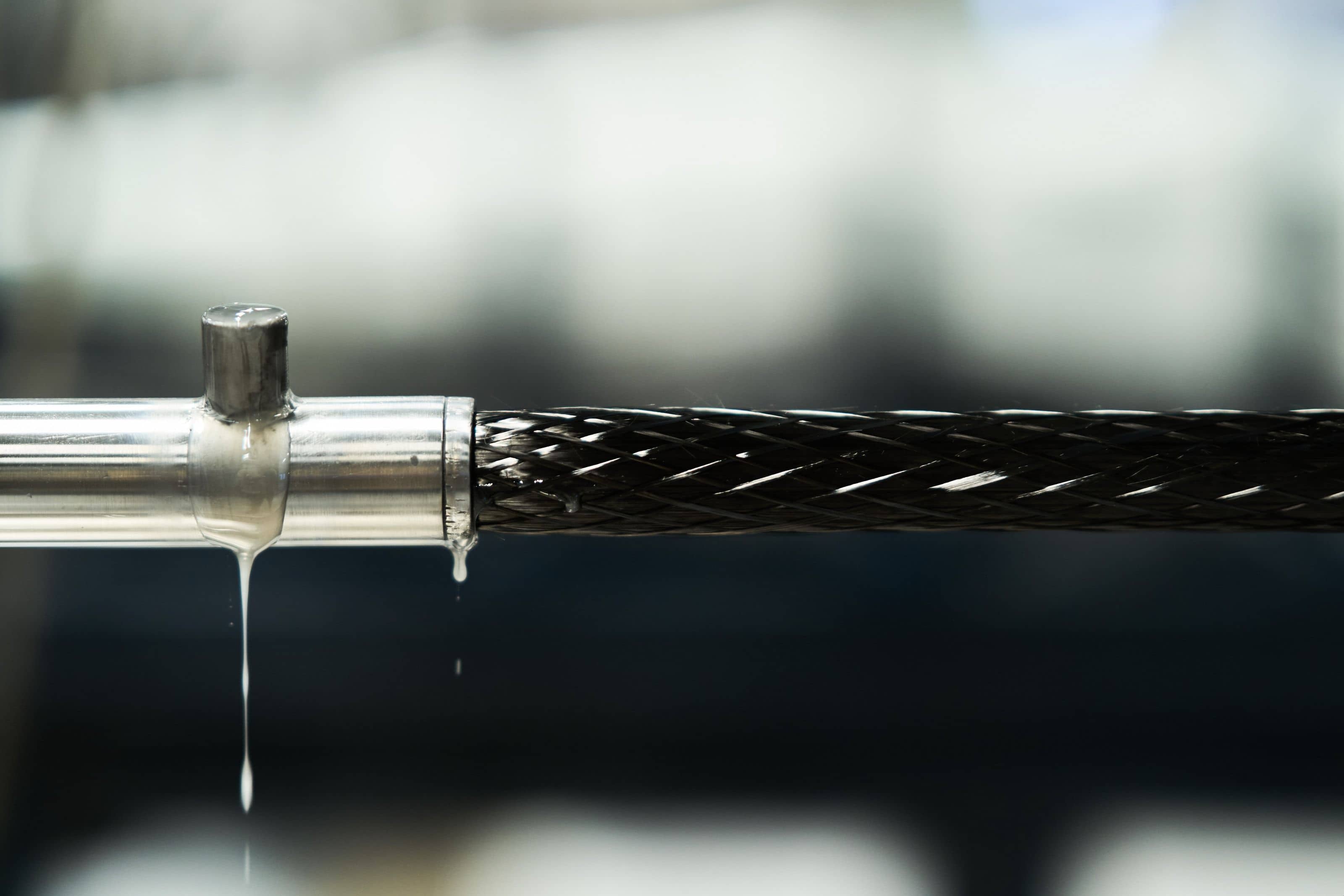 A braided carbon-fibre profile being pulled through a metal die, wet resin dripping from the tooling