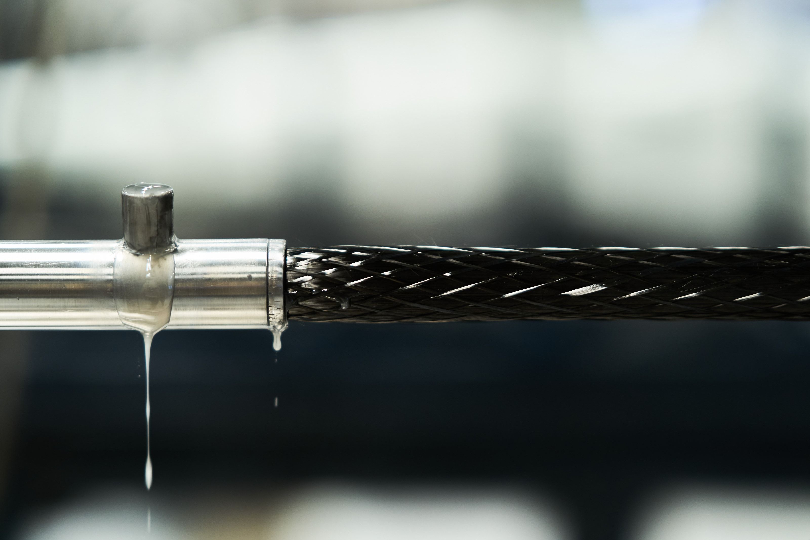 A braided carbon-fibre profile being pulled through a metal die, wet resin dripping from the tooling