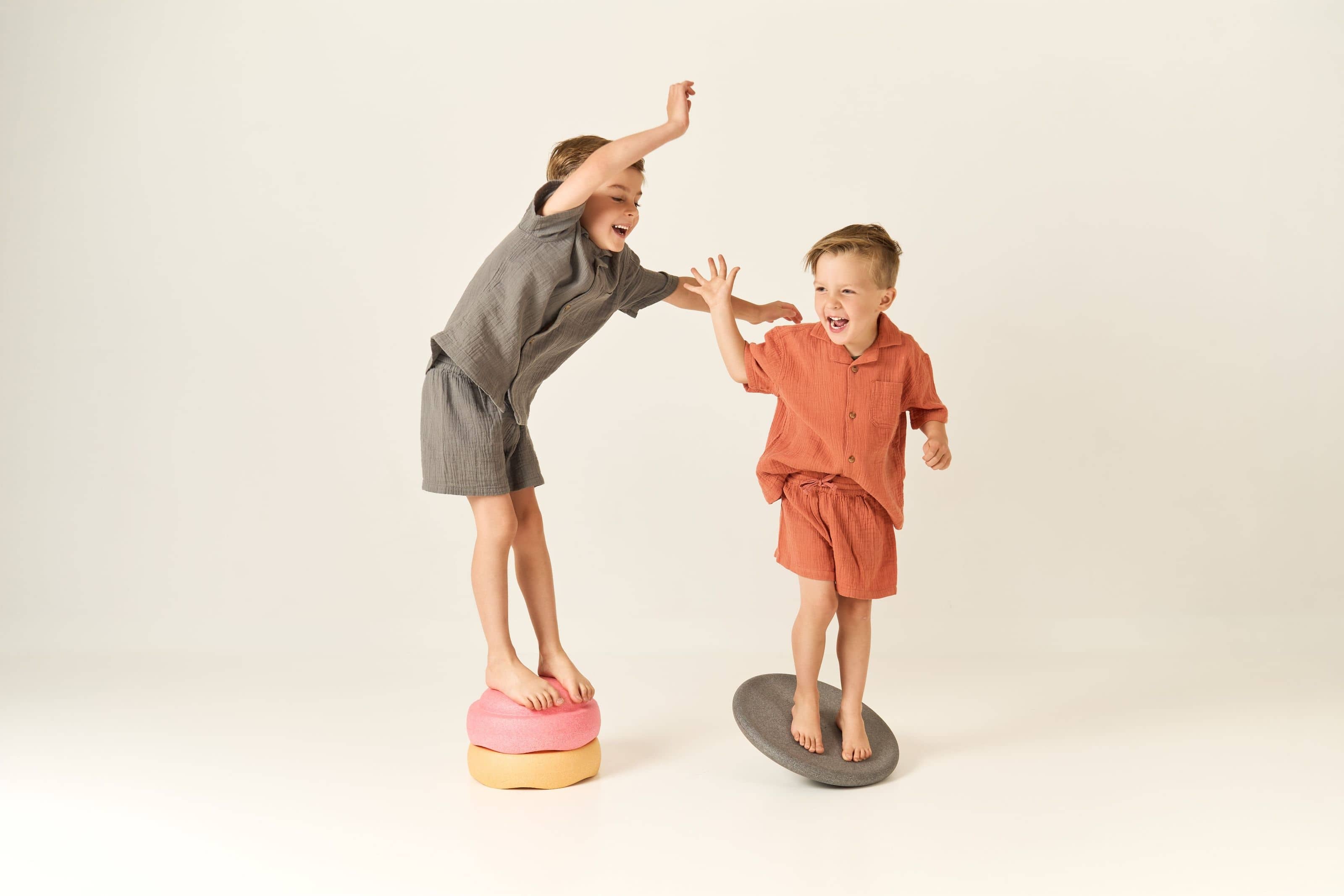 Two children balancing barefoot on foam stepping stones, laughing and reaching out to steady each other