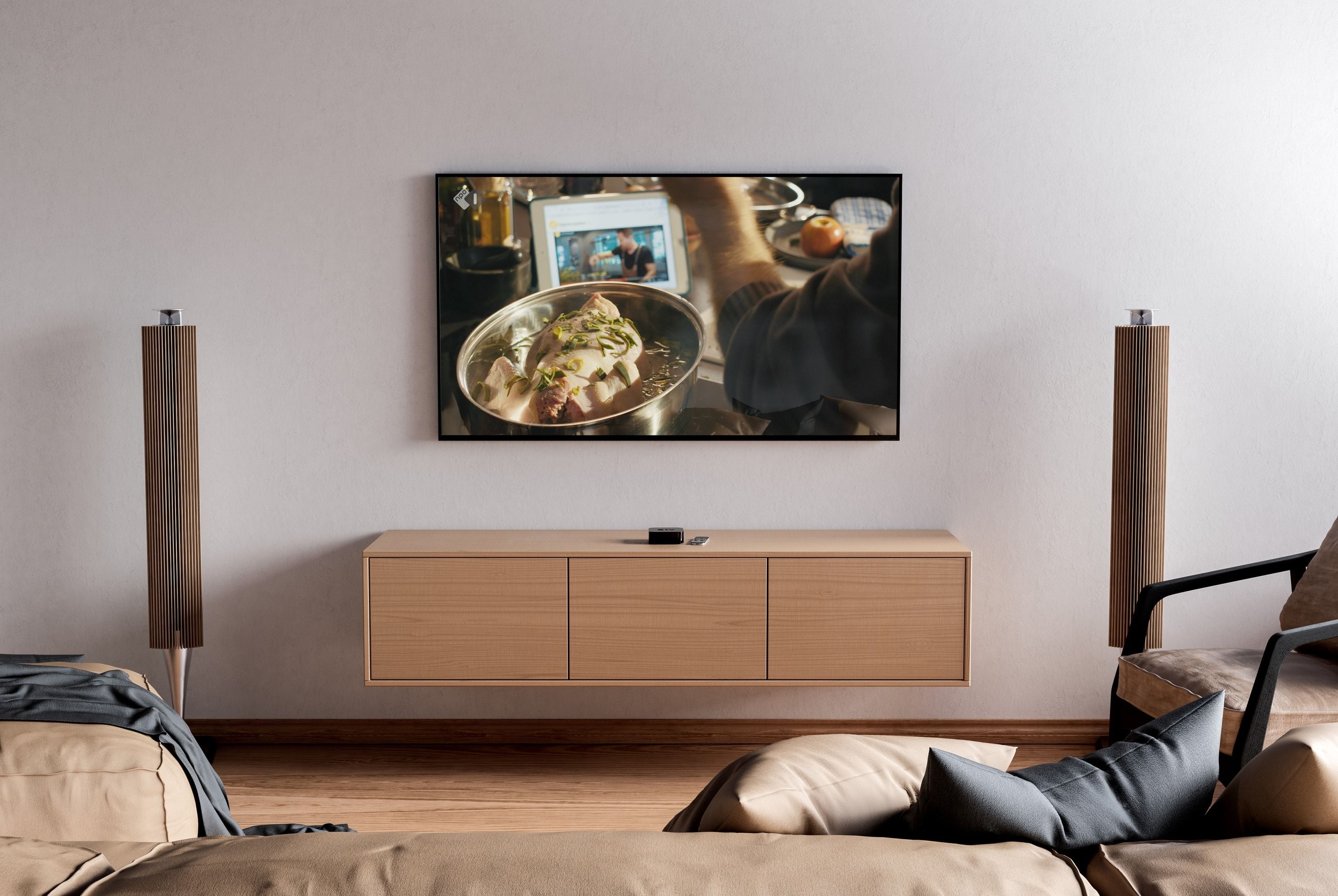 The Nepluvi commercial playing on a wall-mounted television in a living room, a whole chicken poaching in a pan with leek and herbs