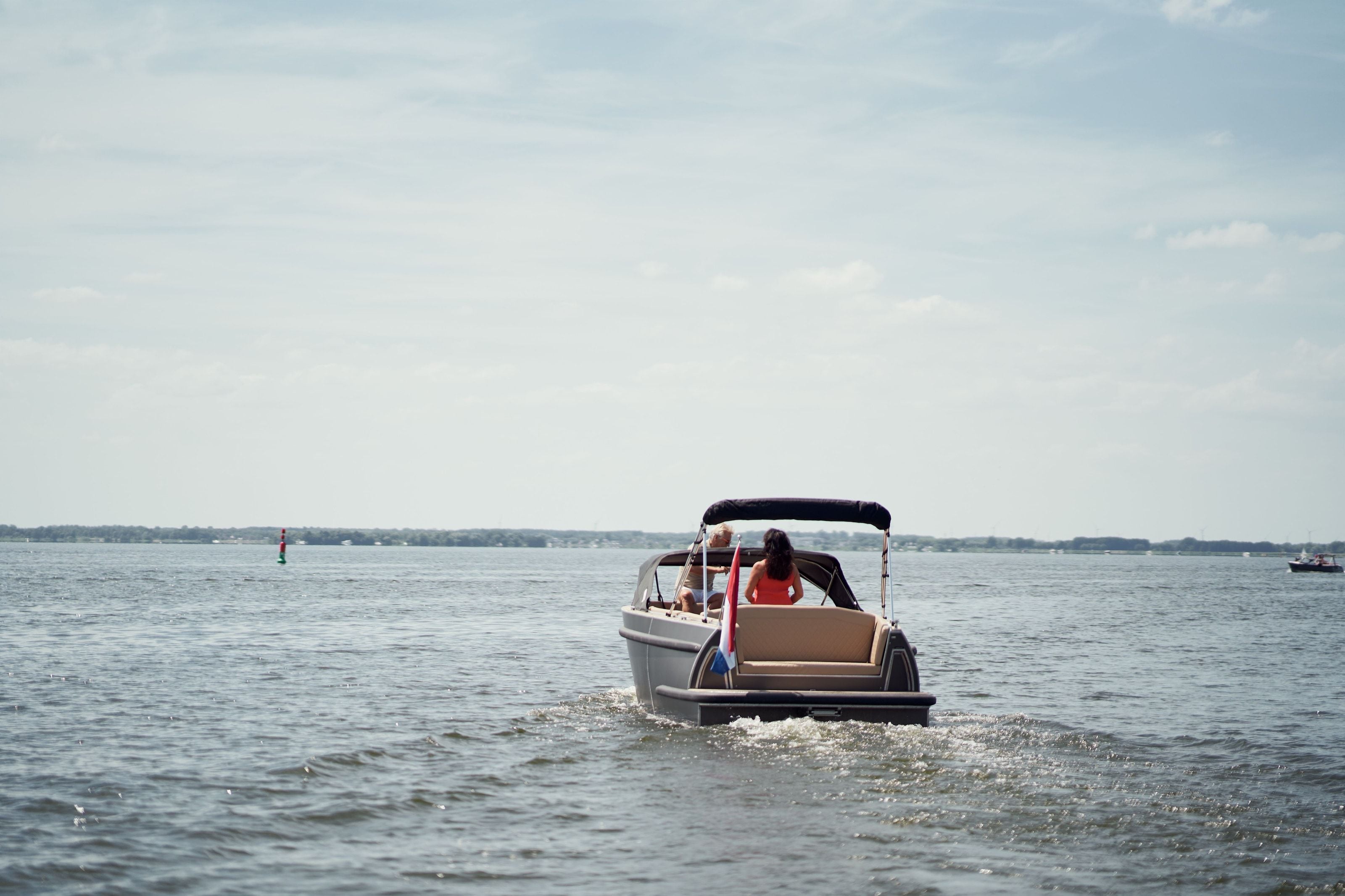 The same electric boat seen from behind, two people aboard, out on the open water of the Veluwemeer under a wide sky