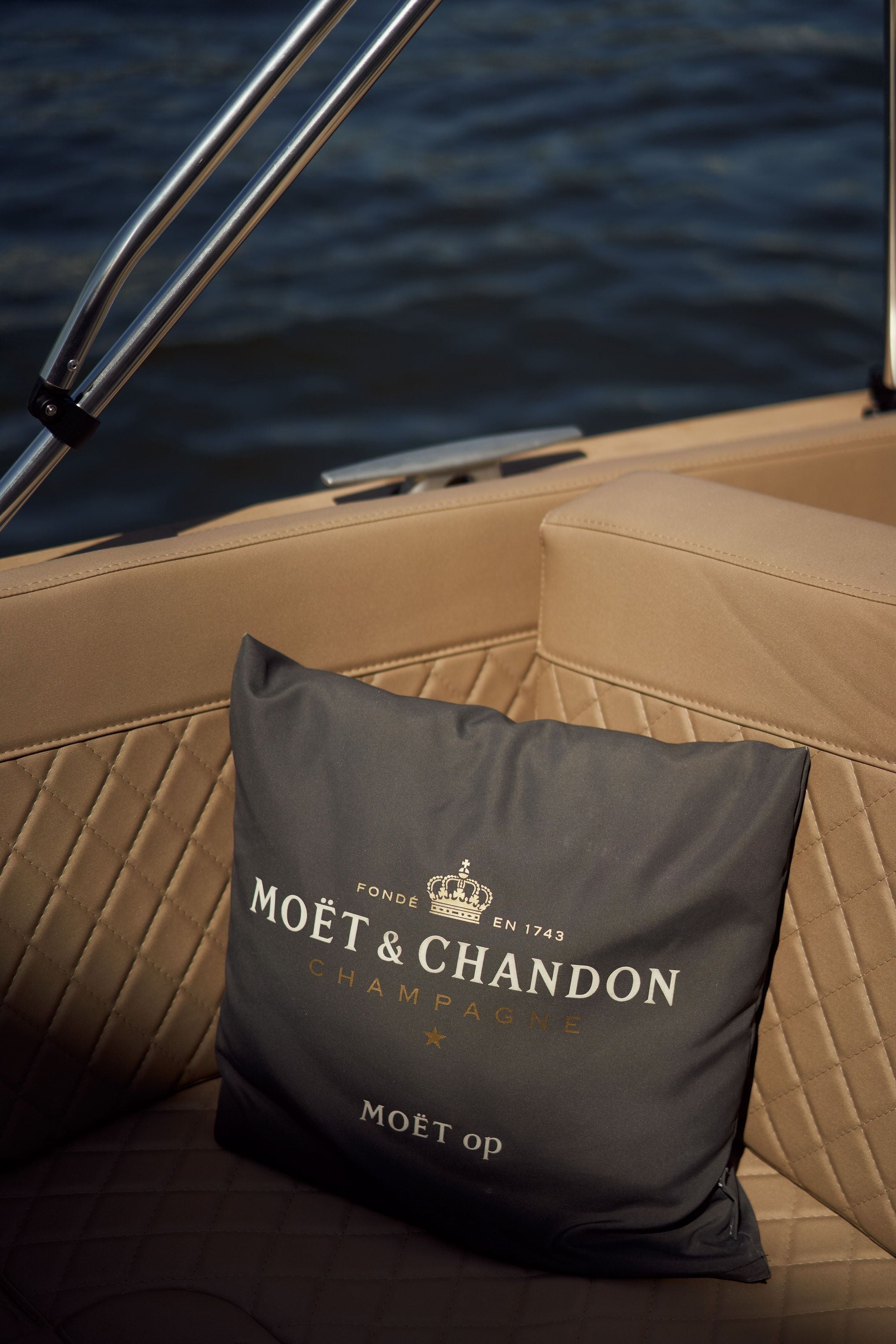A Moët & Chandon cushion on the tan seating of the electric boat, dark water and a cleat behind it