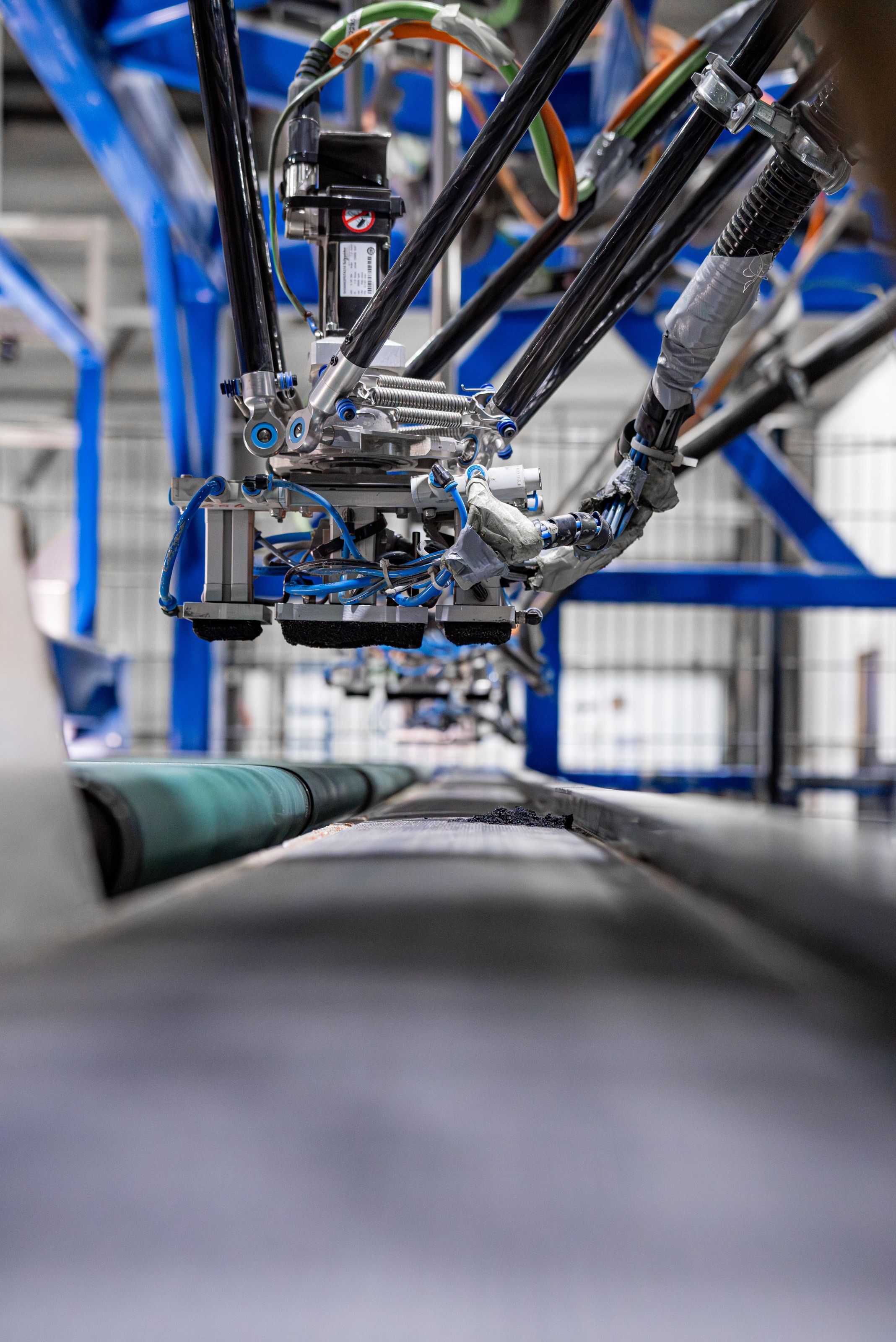 A robotic gripper arm lifting a finished composite profile off a production line, blue machine framework overhead