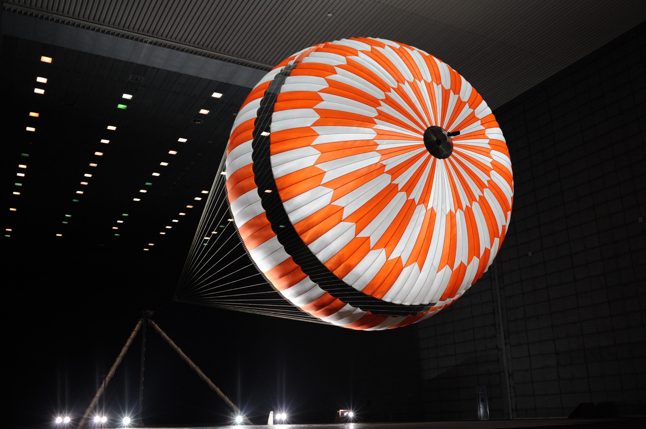 A NASA test rig at night, the orange and white Mars 2020 landing parachute fully inflated overhead, its suspension lines strung with Teijin Aramid’s Technora fibre