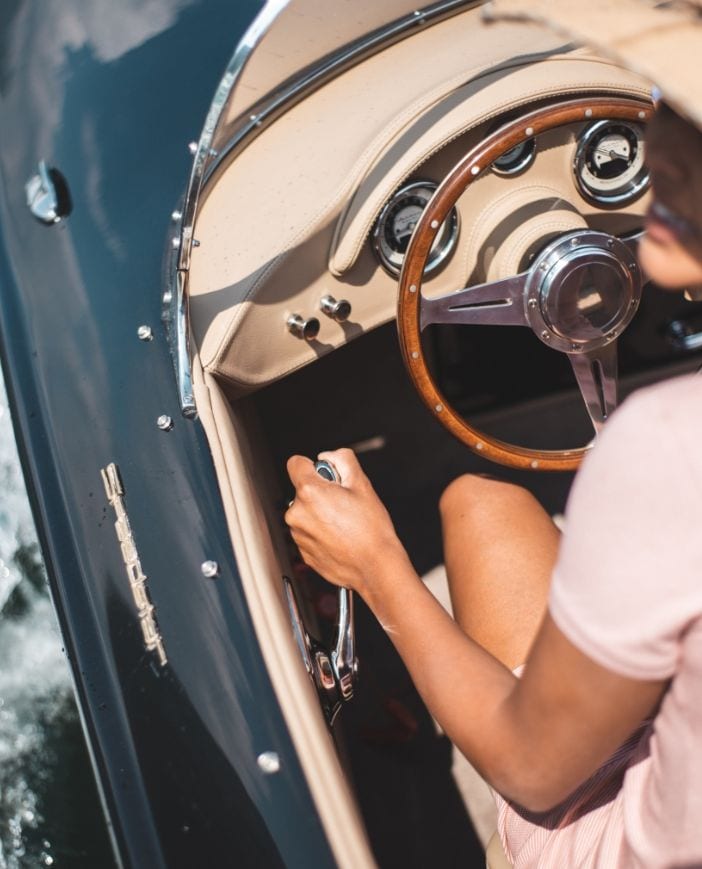 The cockpit of a dark blue Hermes Speedster under way, a woman at its wooden steering wheel