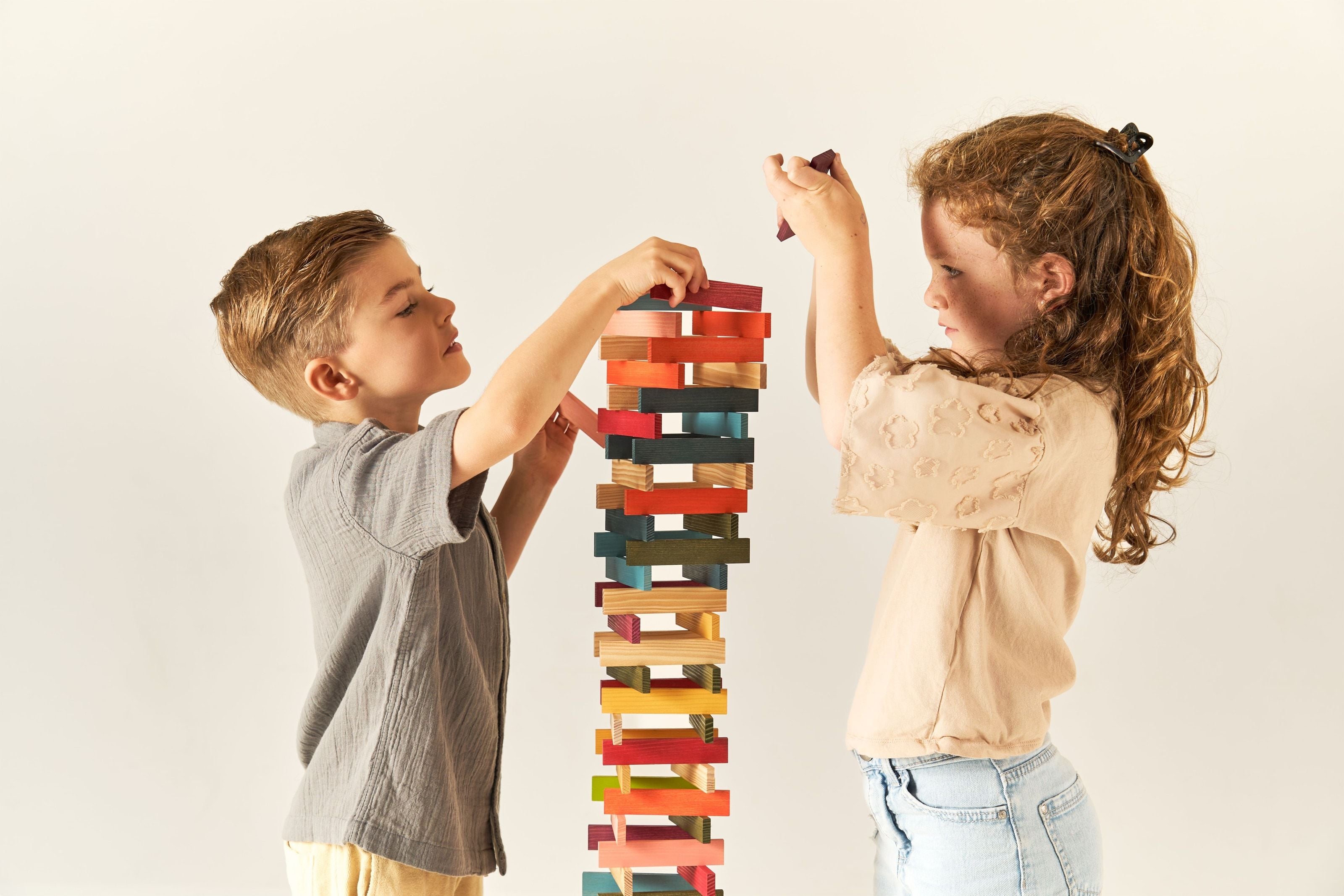 Two children building a tall tower of coloured wooden blocks between them, each placing pieces from their own side